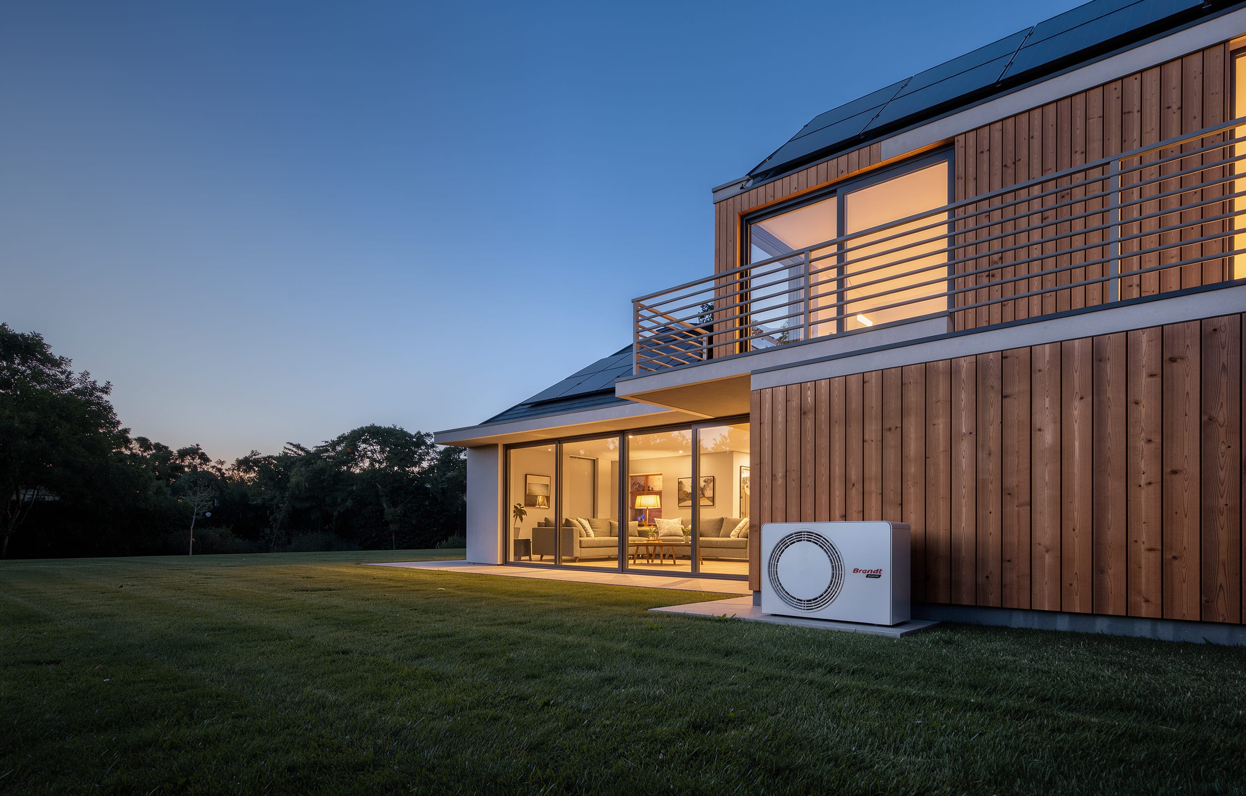 Maison à bardage bois au crépuscule, équipée de panneaux solaires et d’une pompe à chaleur Brandt Energy